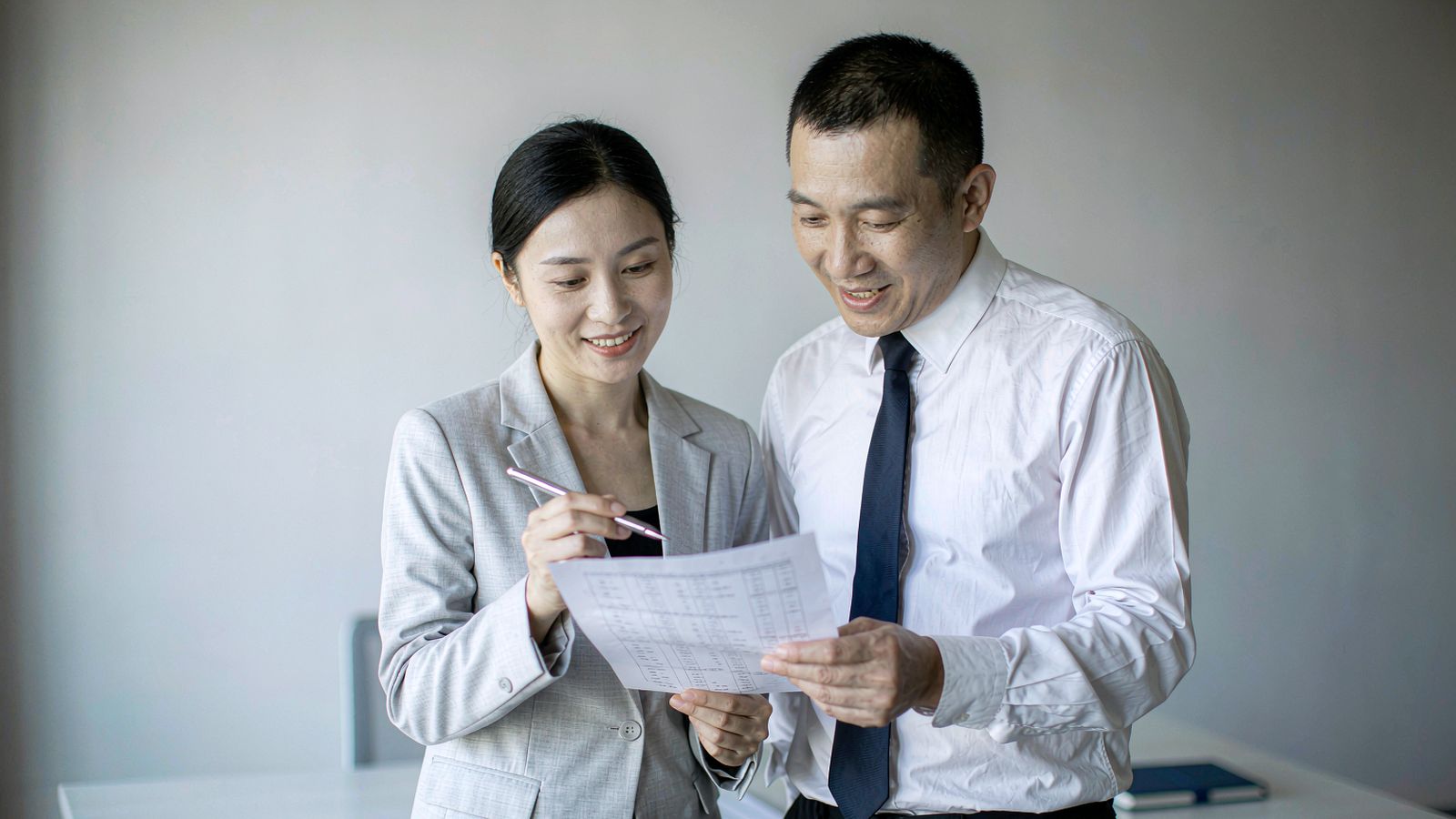 Two colleagues checking a document line by line at a desk